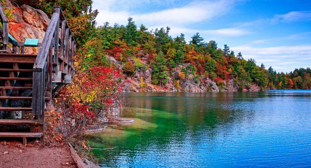 Vue d'un lac paisible entouré par la forêt dense et les collines du Parc de la Gatineau.